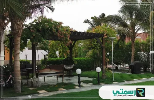 منطقة جلوس خارجية مغطاة ببرجولا خشبية في حديقة مُضاءة.