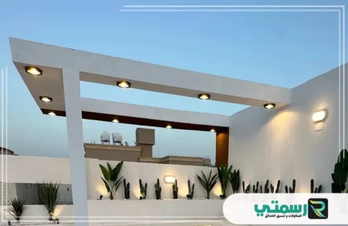 منطقة جلوس خارجية ذات تصميم معماري حديث باللون الأبيض وإضاءة مدمجة ونباتات صحراوية.